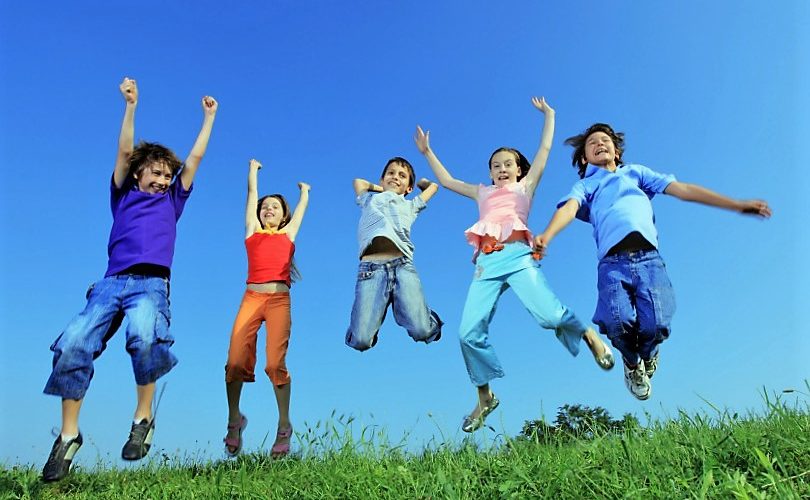 Group of five happy children jumping on meadow.